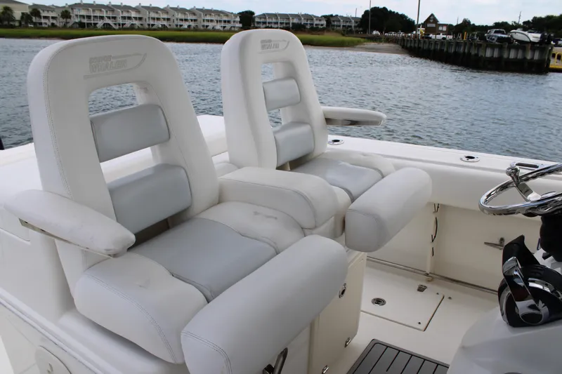 Slide: The Image of 2015 Boston Whaler 320 Outrage boat with white cushioned seats and steering wheel, dockside view. - 45