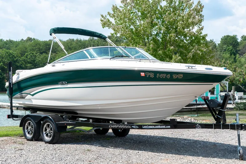 The Image of 2002 Sea Ray 230 Bow Rider boat on trailer, parked near a lake with trees. - 1