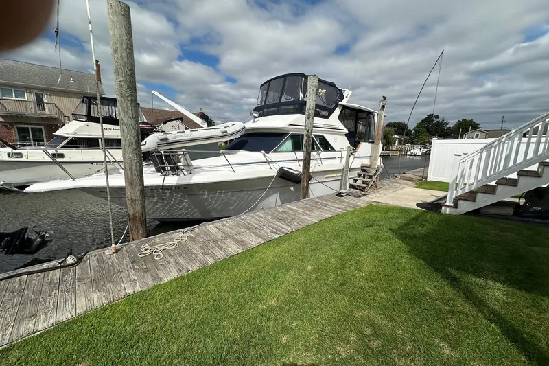 The Image of 1989 Sea Ray 380 Aft Cabin yacht docked by a wooden pier under cloudy skies. - 1