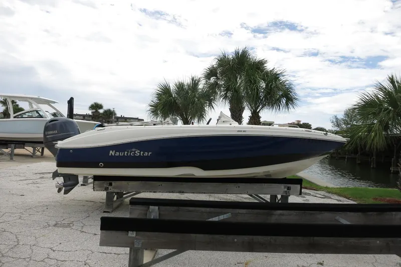 Slide: The Image of 2015 NauticStar 203SC Sport Deck boat on trailer, parked near palm trees and water. - 40