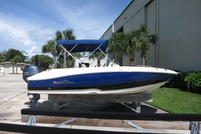 The Image of 2015 NauticStar 203SC Sport Deck boat with blue hull, docked near palm trees. - 5