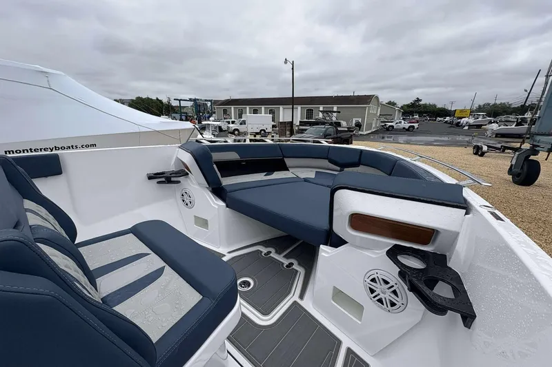 Slide: The Image of 2026 Monterey 27 Elite boat interior with blue seating and cup holders, parked outdoors. - 5