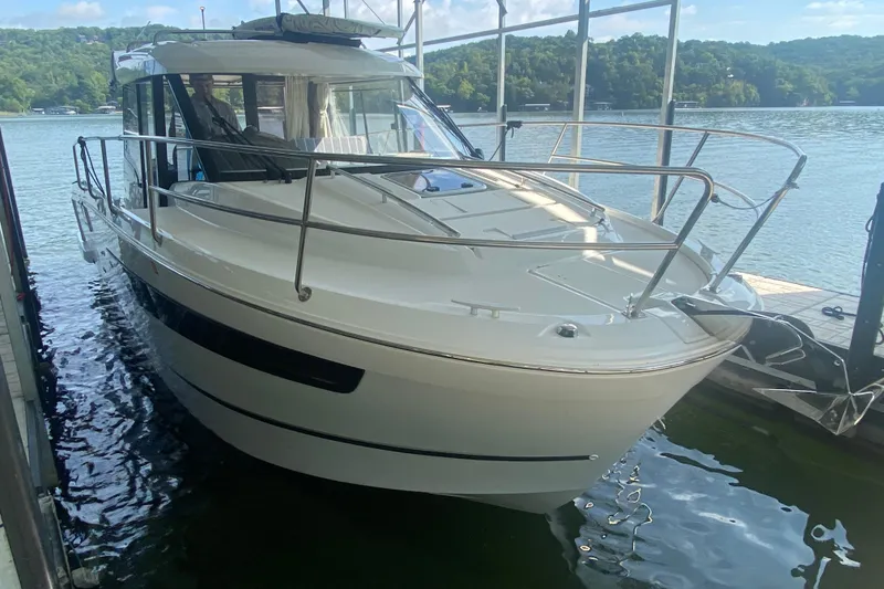 Slide: The Image of 2024 Jeanneau NC 895 boat docked on a serene lake with lush green hills. - 14