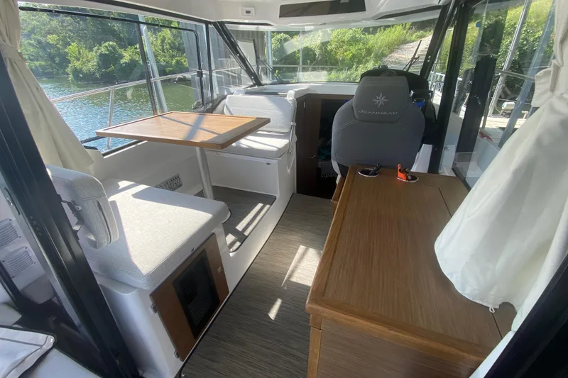 Slide: The Image of 2024 Jeanneau NC 895 interior with seating, table, and helm, overlooking water. - 15