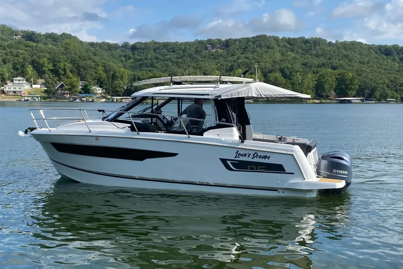 Slide: The Image of 2024 Jeanneau NC 895 boat on a serene lake with lush green hills. - 3