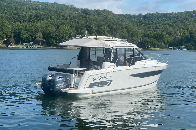 Slide: The Image of 2024 Jeanneau NC 895 boat on a serene lake with lush green shoreline. - 5