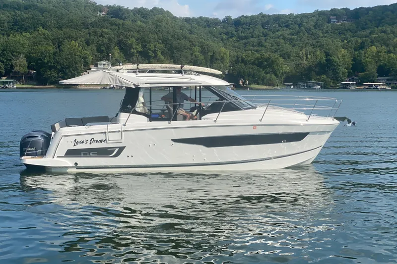 Slide: The Image of 2024 Jeanneau NC 895 boat on a serene lake with lush green hills. - 6