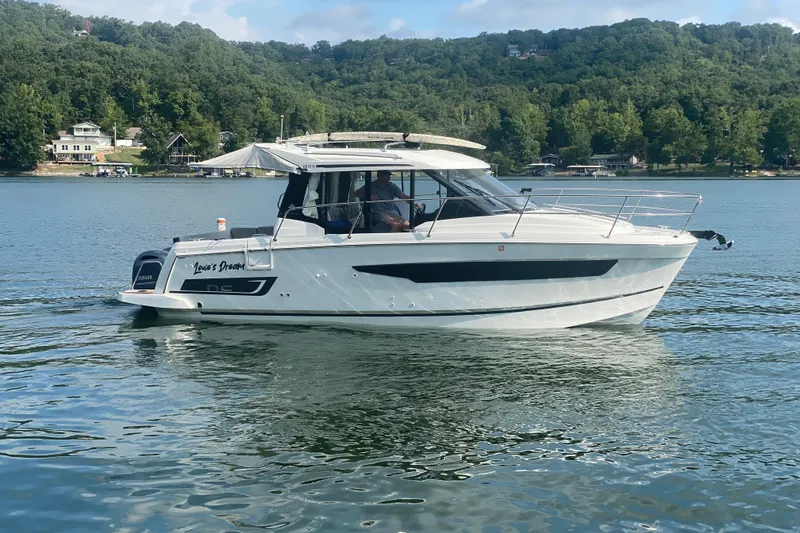 Slide: The Image of 2024 Jeanneau NC 895 boat cruising on a serene lake with lush green hills. - 7