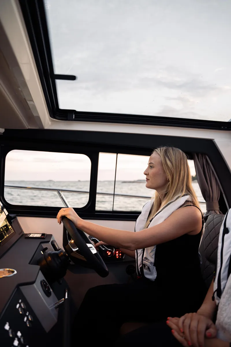 Slide: The Image of Woman steering 2025 Aquador 300 HT boat, interior view, ocean in background. - 14