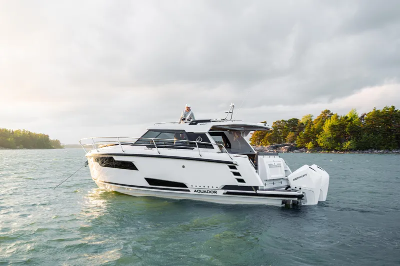Slide: The Image of 2025 Aquador 300 HT yacht on serene water with lush green shoreline. - 6