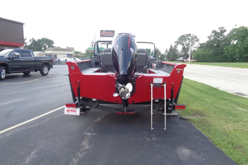 Slide: The Image of 2026 Lund 1800 Explorer Sport boat, red exterior, parked on pavement near grassy area. - 6