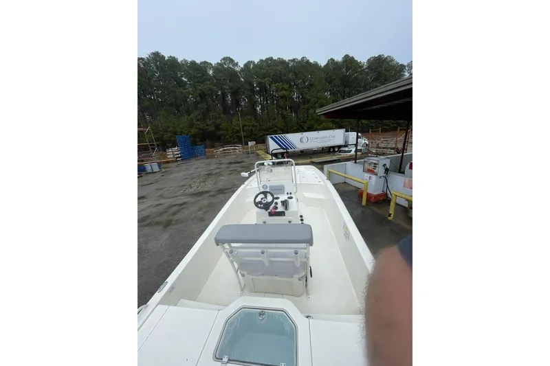 Slide: The Image of 2024 Mako Pro Skiff 19 CC boat in a yard with trees and a truck. - 6