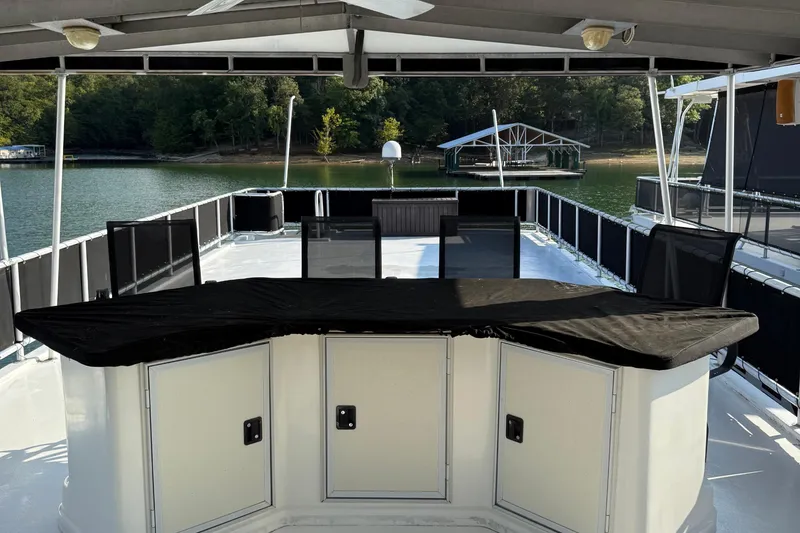 Slide: The Image of 2002 Navigator houseboat deck with covered seating, surrounded by serene lake and trees. - 11