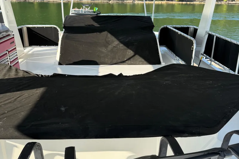 Slide: The Image of 2002 Navigator houseboat deck with black covers, overlooking calm water. - 25