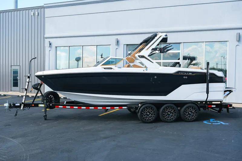 Slide: The Image of 2026 MasterCraft XStar 25 boat on trailer, parked outside a building. - 2