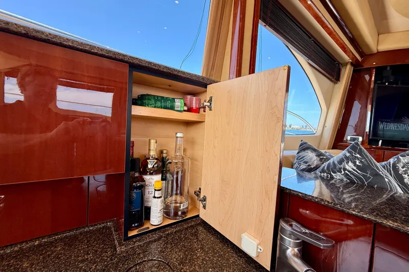 Slide: The Image of 2007 Sea Ray 52 Sedan Bridge interior with open cabinet displaying liquor bottles. - 76
