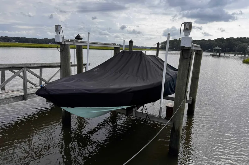 Slide: The Image of Covered 2021 Bulls Bay 2200 boat on a lift by a wooden dock, under cloudy skies. - 29