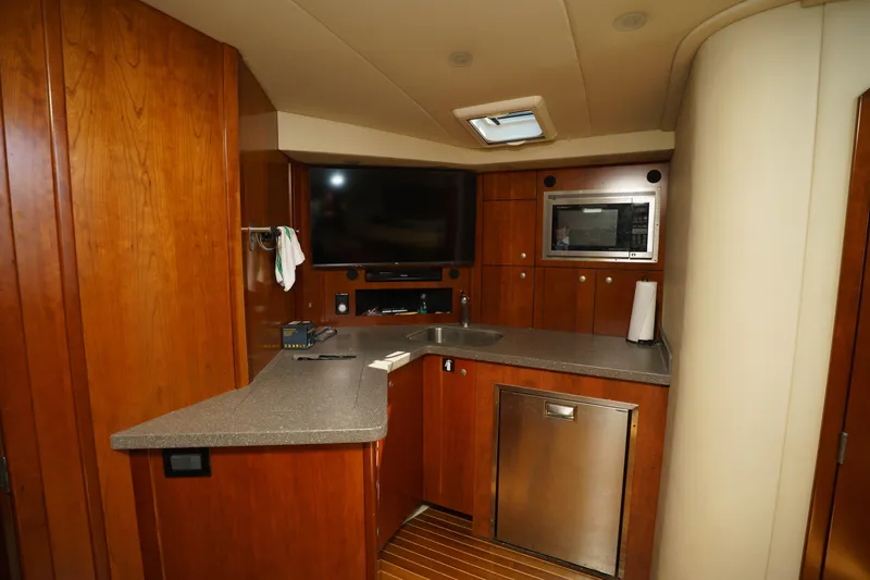 Slide: The Image of 2011 Rampage 41 Express yacht interior with kitchenette, TV, and wooden cabinetry. - 13