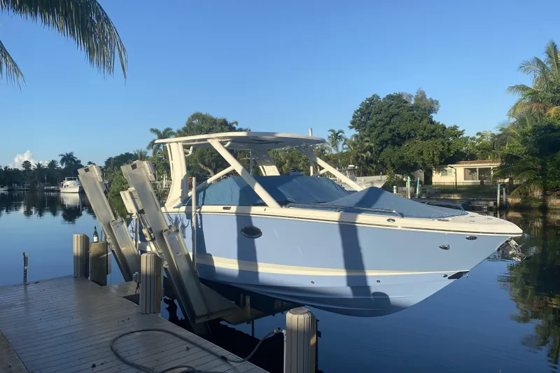 Slide: The Image of 2022 Chaparral 280 OSX boat docked on a serene waterfront with lush greenery. - 2