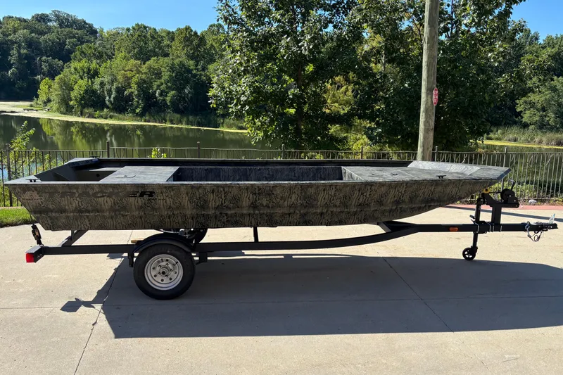 The Image of 2026 Tracker Grizzly 1648 Utility boat on trailer, parked near a scenic lake. - 0