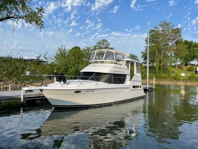 The Image of 1998 Carver 355 Aft Cabin Motor Yacht docked on a serene lake under a blue sky. - 0