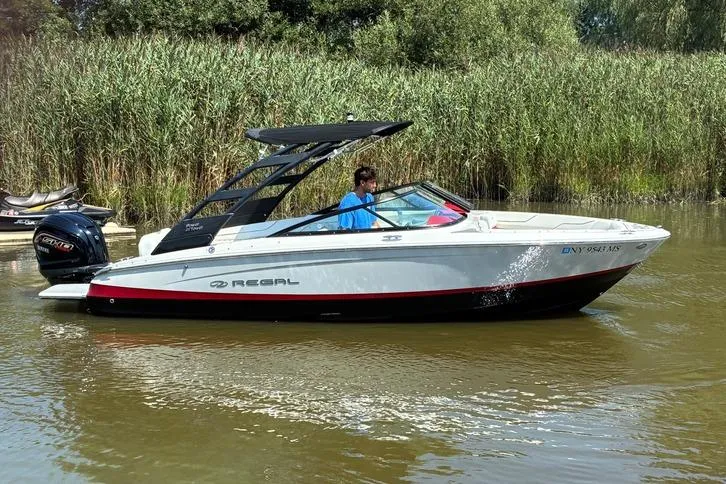Slide: The Image of 2022 Regal LX2 boat cruising on a calm river with lush greenery in the background. - 2