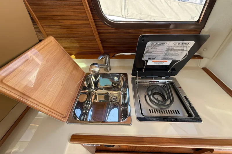 Slide: The Image of 2026 Ranger Tugs R-25 kitchen with sink and stove, featuring wood accents. - 13