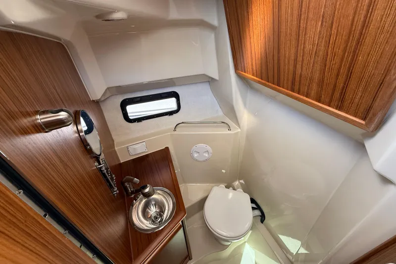 Slide: The Image of 2026 Ranger Tugs R-25 boat bathroom with wood accents, sink, and toilet. - 19