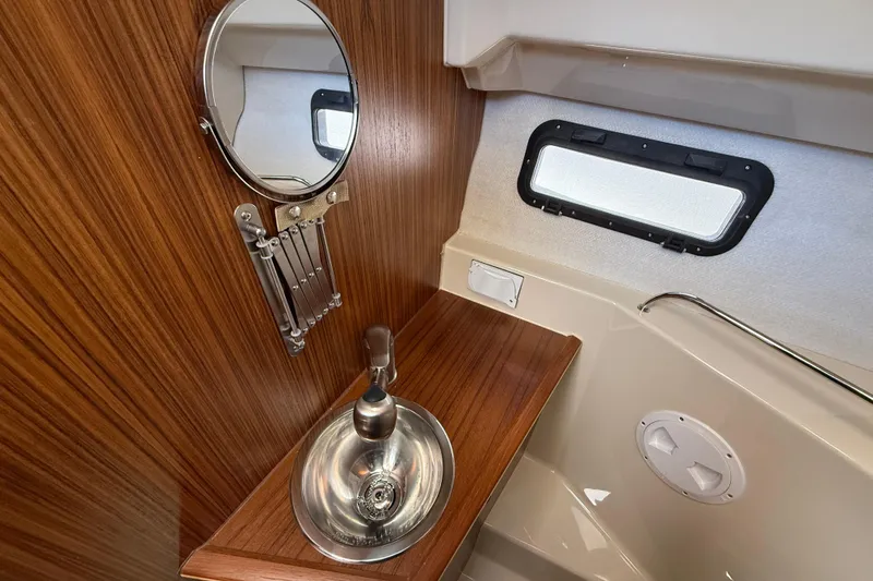 Slide: The Image of 2026 Ranger Tugs R-25 bathroom with wood paneling, round mirror, and stainless steel sink. - 20