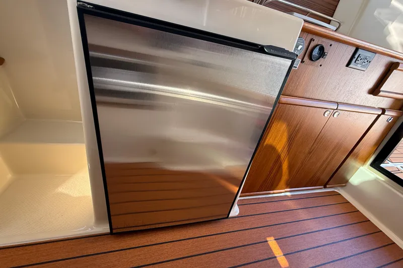 Slide: The Image of 2026 Ranger Tugs R-25 interior with stainless steel fridge and wooden cabinetry. - 22