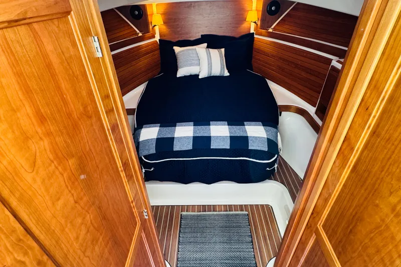 Slide: The Image of 2025 Back Cove 34O cabin interior with cozy bed and wooden accents. - 2