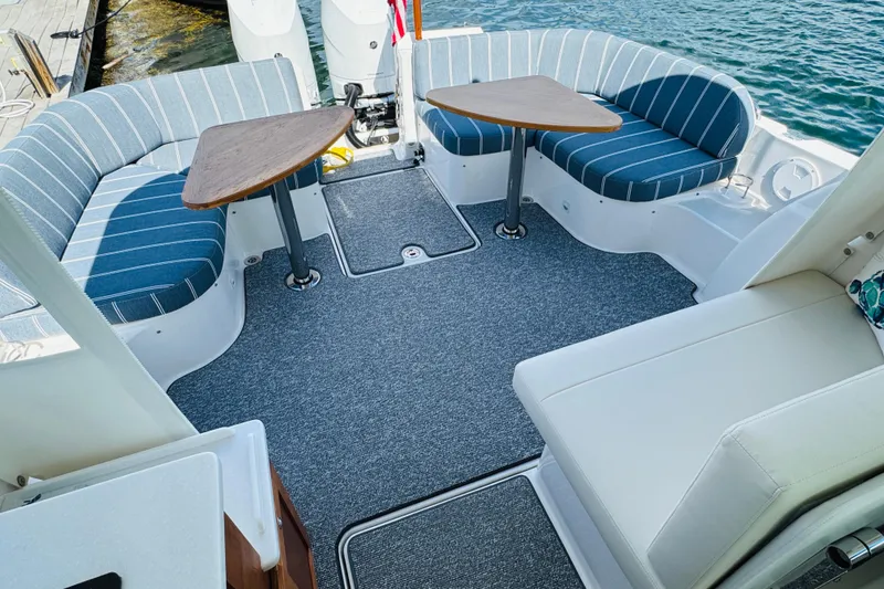 Slide: The Image of 2025 Back Cove 34O boat interior with striped seating and dual tables on a sunny day. - 28
