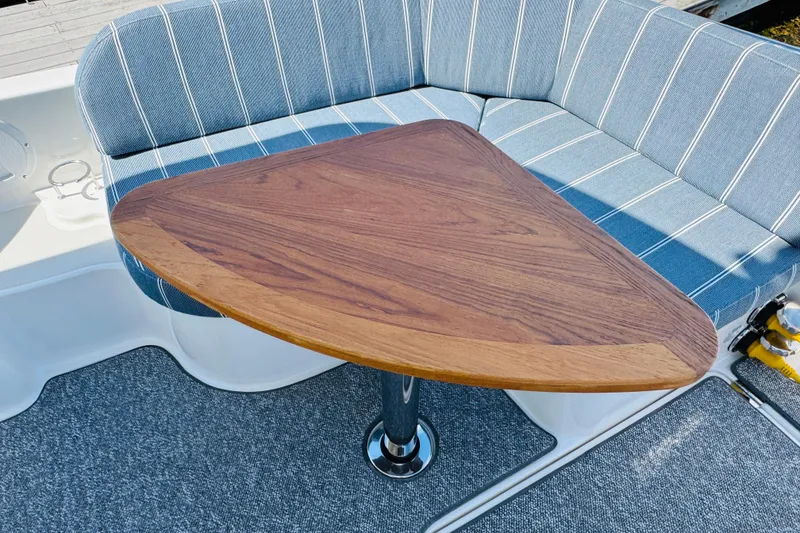 Slide: The Image of 2025 Back Cove 34O boat interior with triangular wooden table and striped seating. - 31