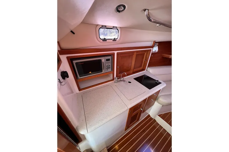 Slide: The Image of 2009 MJM 29z Express boat interior with kitchenette, featuring microwave, sink, and wooden cabinetry. - 18