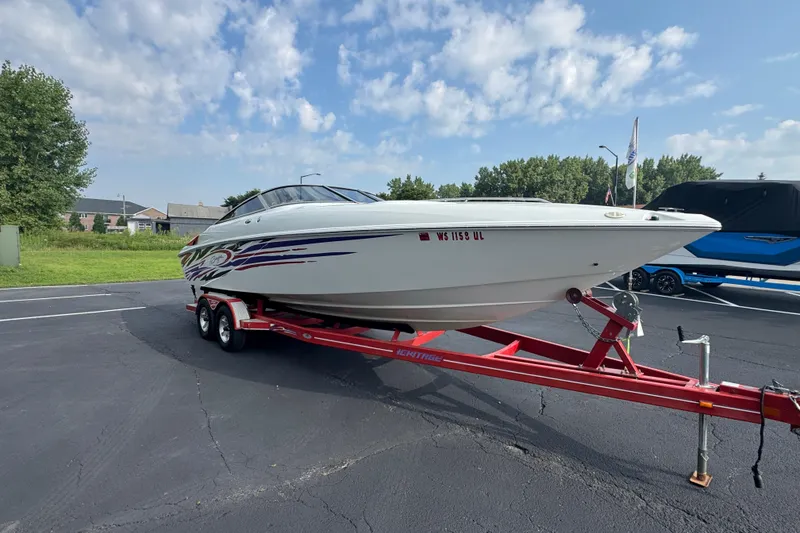 Slide: The Image of 2004 Baja 275 boat on red trailer, parked outdoors under a partly cloudy sky. - 3