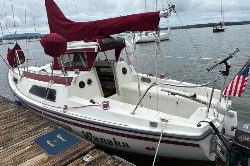 The Image of 1983 Sonic 23 sailboat docked, featuring maroon sails and American flag. - 0