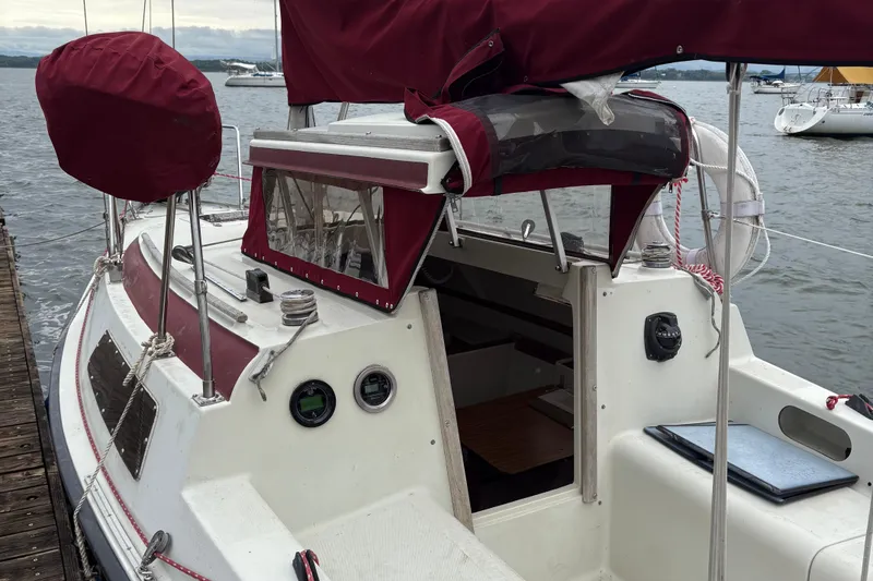 Slide: The Image of 1983 Sonic 23 sailboat with maroon covers docked by the water. - 7