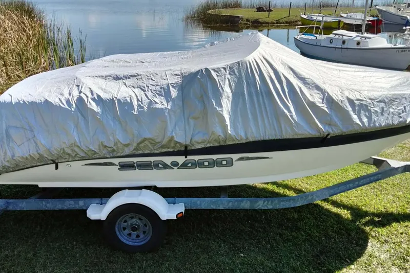 Slide: The Image of 2003 Sea-Doo Utopia 185 boat covered on trailer by a lake. - 26