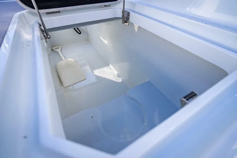 Slide: The Image of 2024 Yellowfin 54 Offshore storage compartment with white interior and shovel. - 38