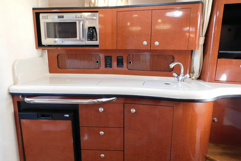 Slide: The Image of 2005 Sea Ray 320 Sundancer galley with microwave, sink, and wooden cabinetry. - 79