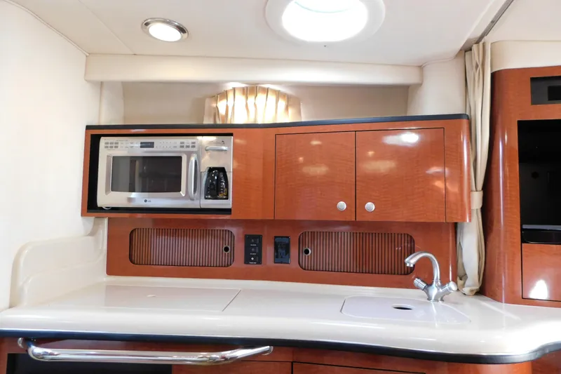 Slide: The Image of 2005 Sea Ray 320 Sundancer galley with microwave, sink, and wooden cabinetry. - 80