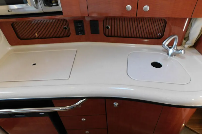 Slide: The Image of 2005 Sea Ray 320 Sundancer galley with sink and countertop, featuring wood cabinetry. - 82
