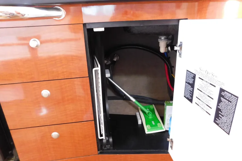 Slide: The Image of Open cabinet in 2005 Sea Ray 320 Sundancer with cleaning supplies and visible plumbing. - 89