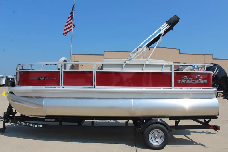 The Image of 2026 Sun Tracker Bass Buggy 18 DLX pontoon boat on trailer, American flag in background. - 1
