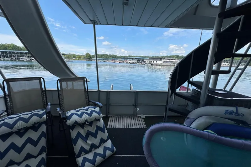 Slide: The Image of 1997 Stardust Cruisers 16x78 houseboat interior with lake view, spiral staircase, and lounge chairs. - 16