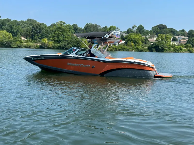 Slide: The Image of 2015 MasterCraft X23 boat cruising on a lake with lush green trees in the background. - 10
