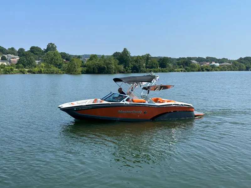 Slide: The Image of 2015 MasterCraft X23 boat cruising on a lake with lush green shoreline. - 14