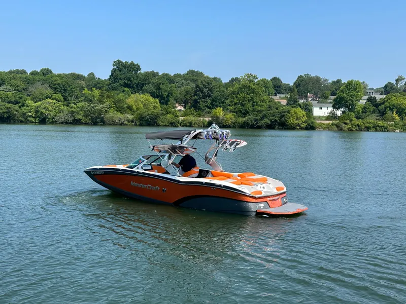 Slide: The Image of 2015 MasterCraft X23 boat cruising on a lake with lush green shoreline. - 6