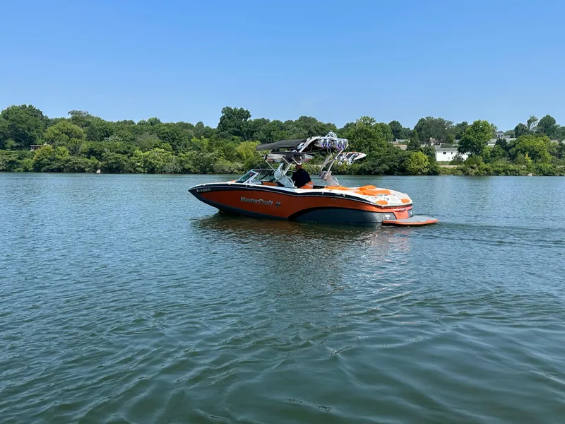 Slide: The Image of 2015 MasterCraft X23 boat cruising on a lake with lush green shoreline. - 8