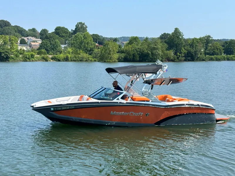 Slide: The Image of 2015 MasterCraft X23 boat on a lake with lush green surroundings. - 9